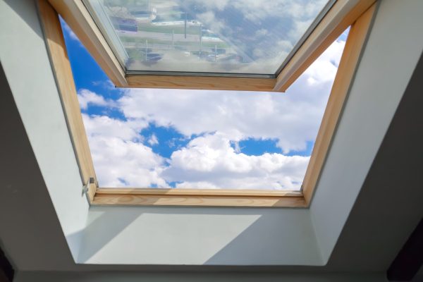 Looking on clouds flying past at the blue sky through open attic window in house roof.